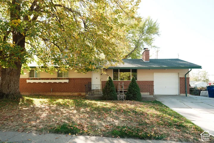 Single-story exterior featuring a combination brick and horizontal siding facade, an attached garage, a brick chimney, and a concrete driveway