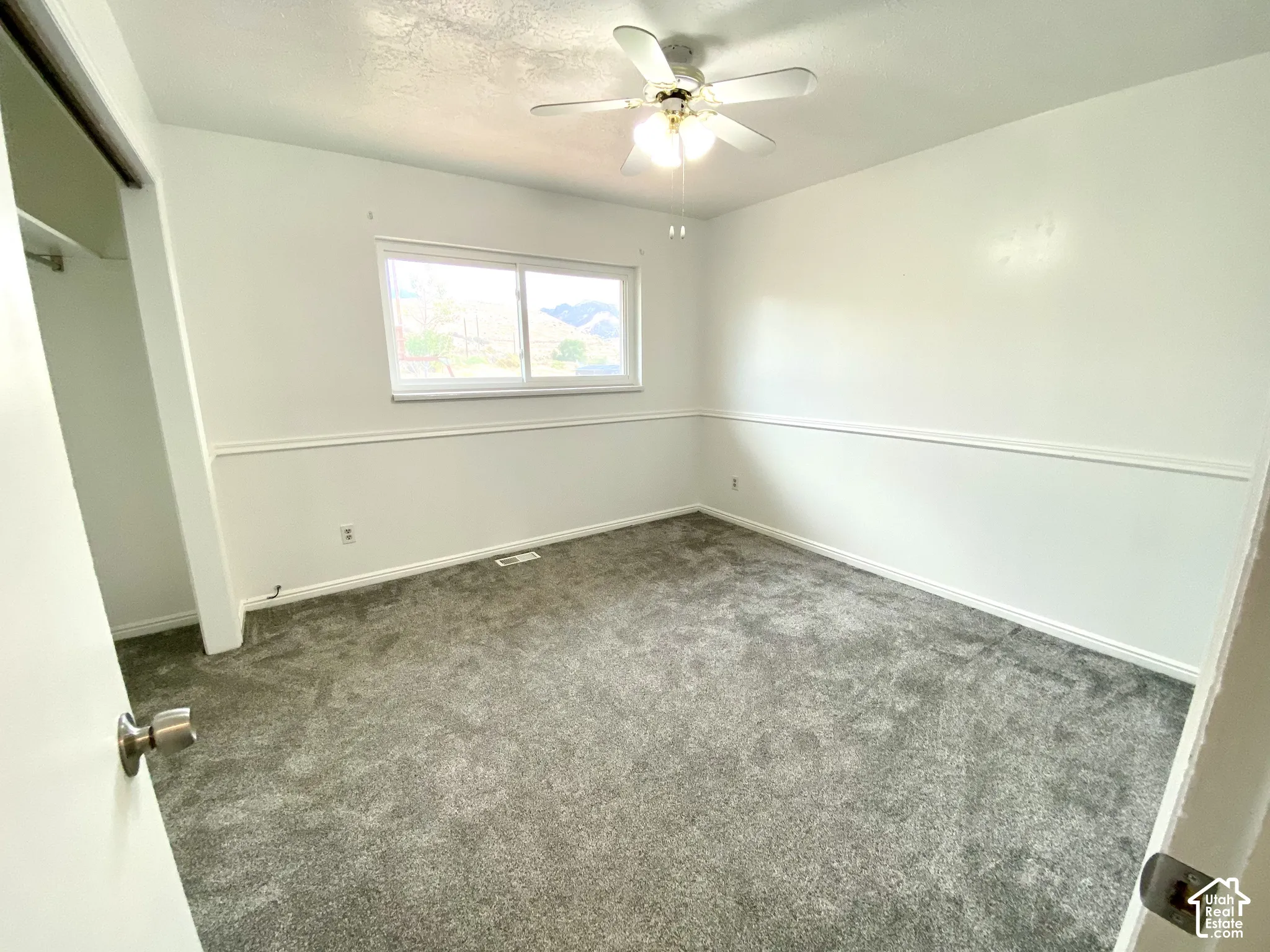 Neutral interior featuring gray carpeting, white chair rail molding, a ceiling-mounted light fixture with fan, and a horizontal sliding window