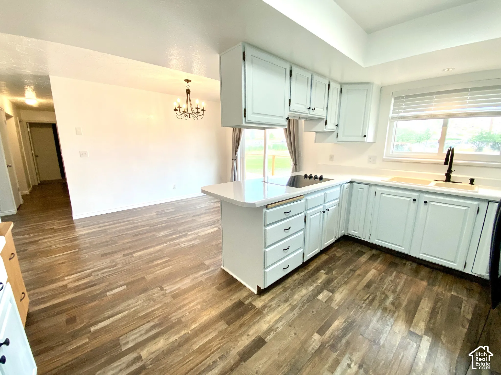 Kitchen featuring wood-finish flooring, light-toned cabinetry, solid surface countertops, an integrated cooktop, and a matte black faucet