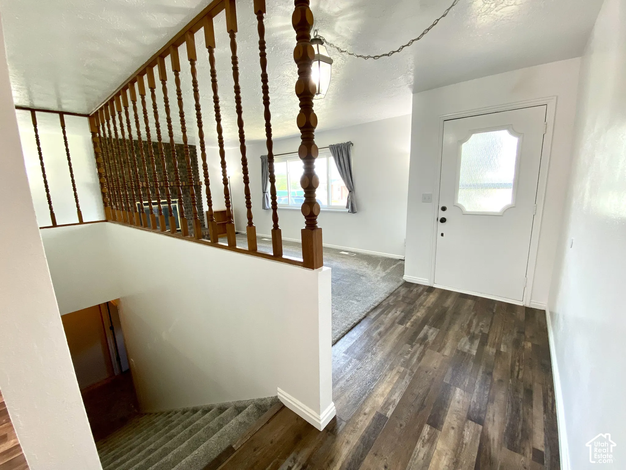 Entryway featuring wood-finish flooring, a turned-wood balustrade, a white front door with decorative glass paneling, and a hanging pendant light