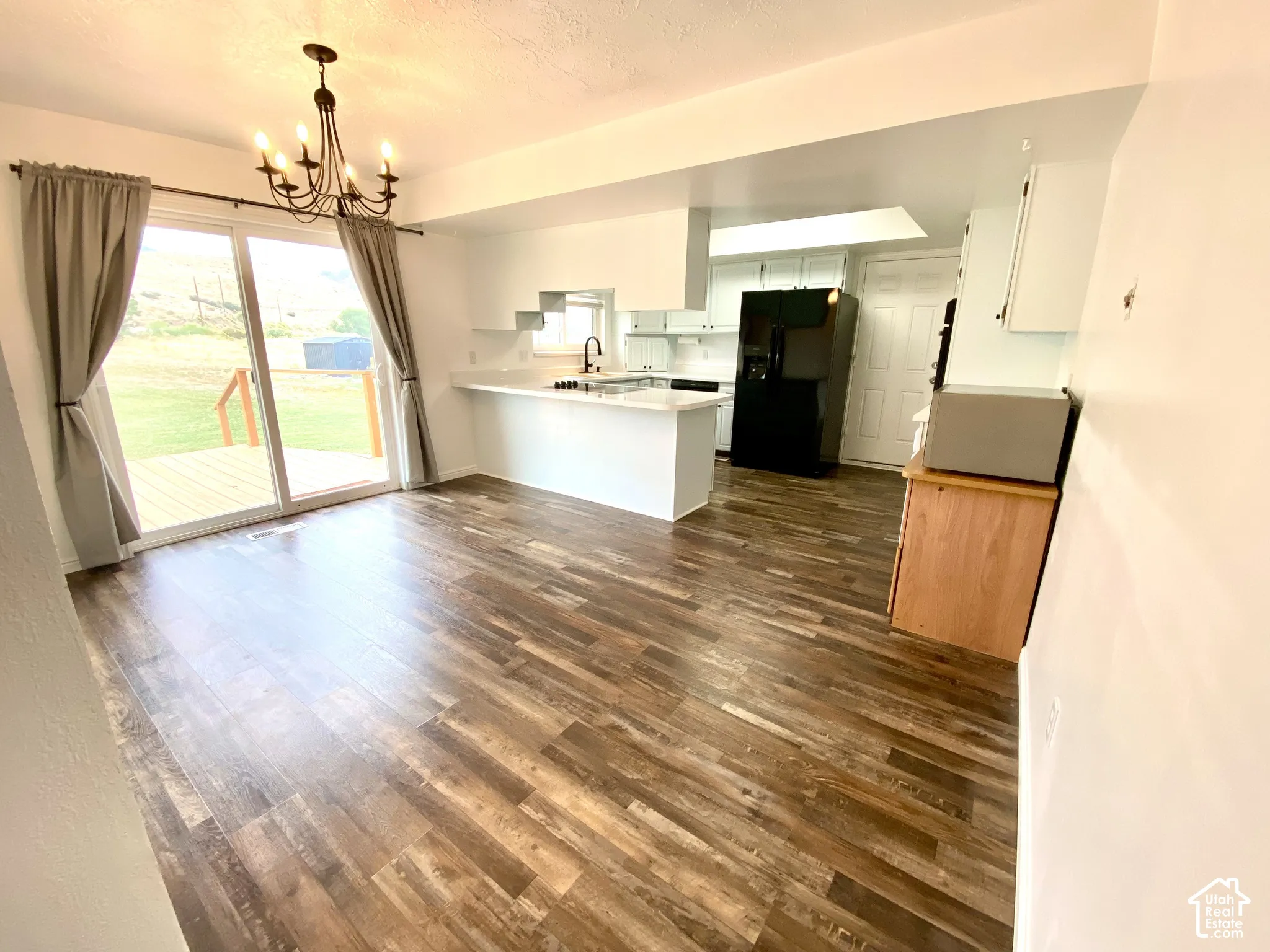 Wood-finish flooring throughout, kitchen featuring white cabinetry, peninsula with white countertops, sliding glass doors, and a decorative iron chandelier