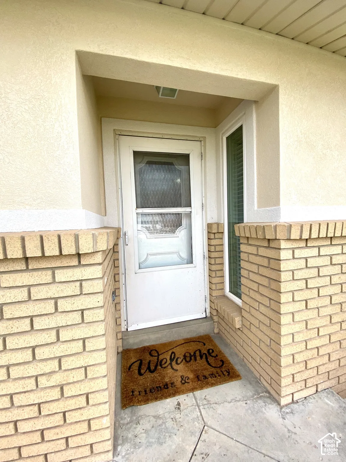 Entryway featuring light-toned brick masonry, stucco siding, a glass-panel storm door, and a full-length sidelight window