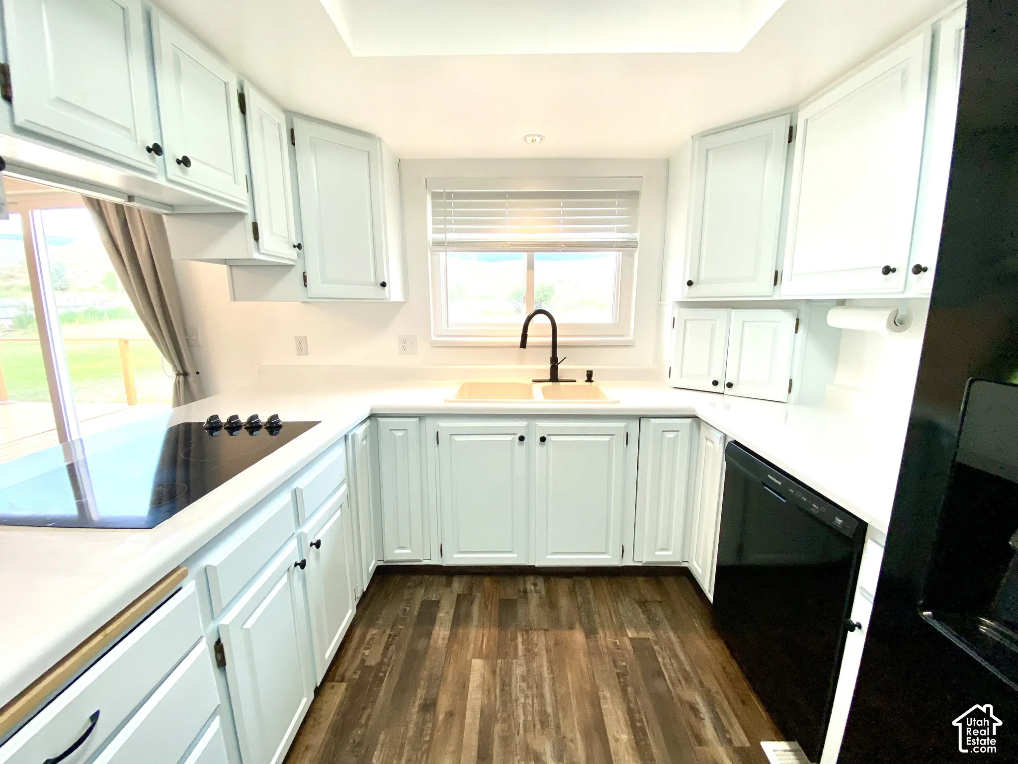 Kitchen featuring white cabinetry, solid surface countertops, wood-finish flooring, dual-basin sink with a matte black faucet, and a black glass cooktop