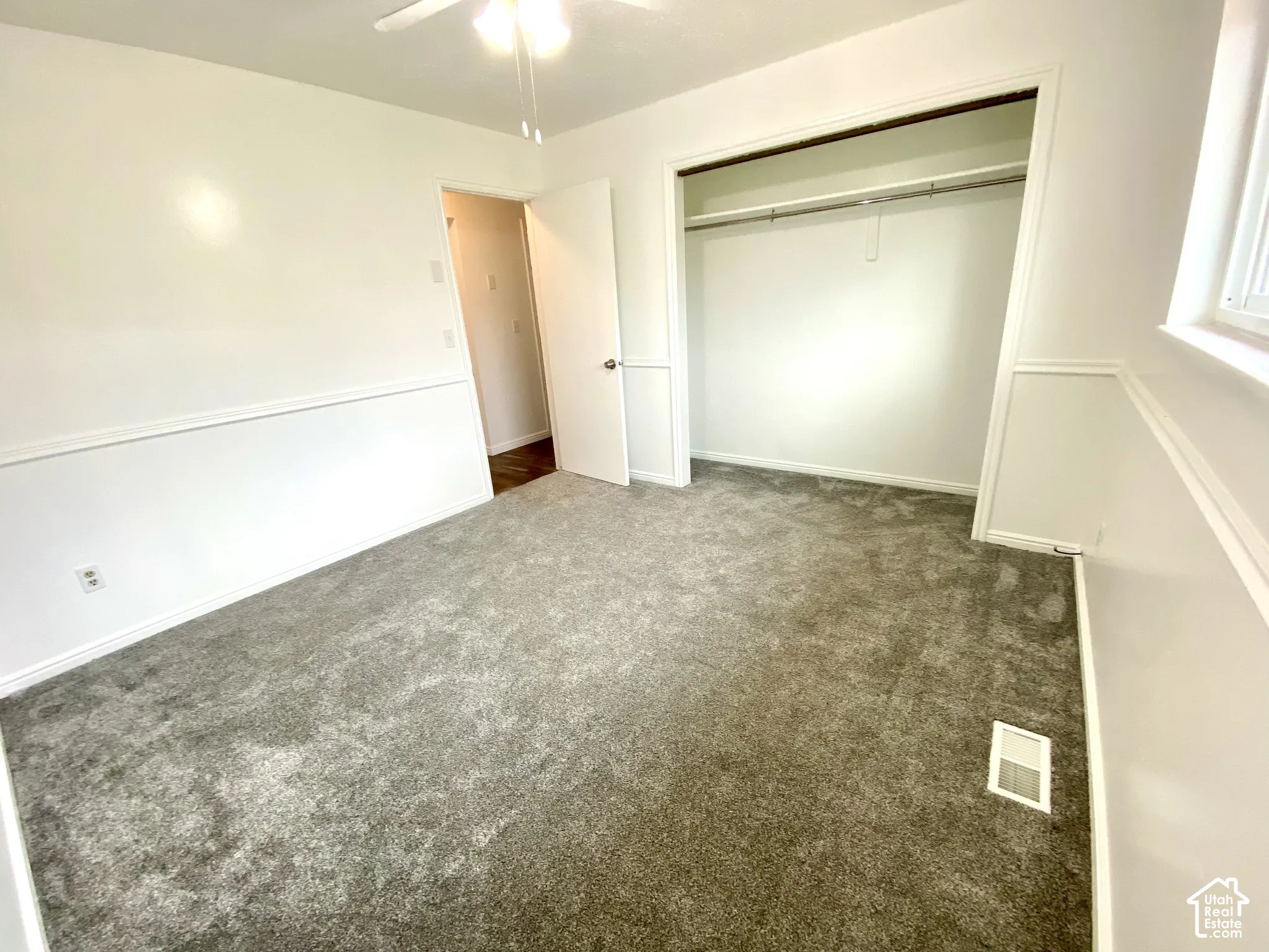 Interior room featuring neutral-toned carpeting, white walls with chair rail molding, a reach-in closet with an integrated rod, and a ceiling-mounted light fixture