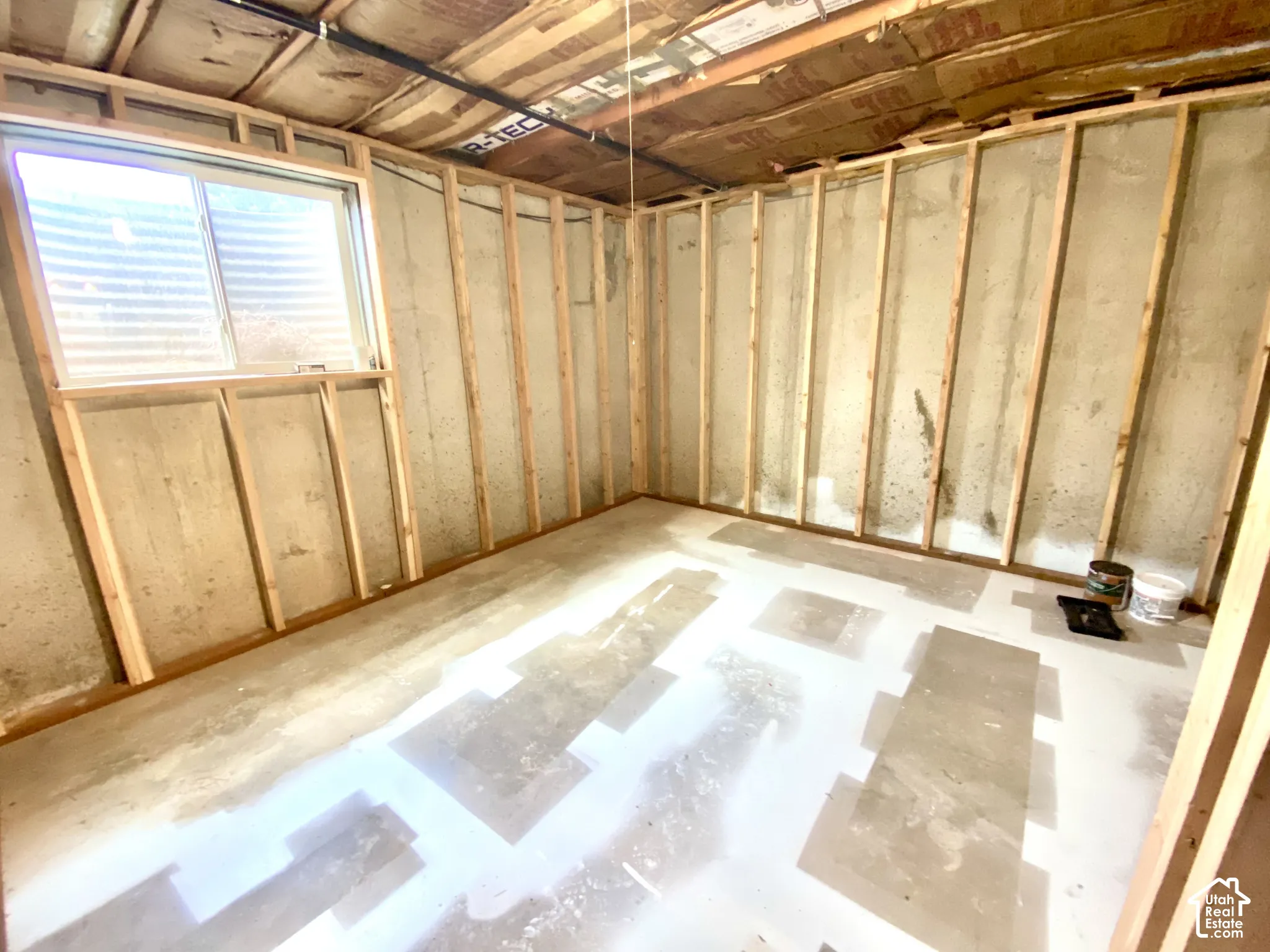 Unfinished space featuring exposed concrete walls, wood stud framing, a slider window, and insulation