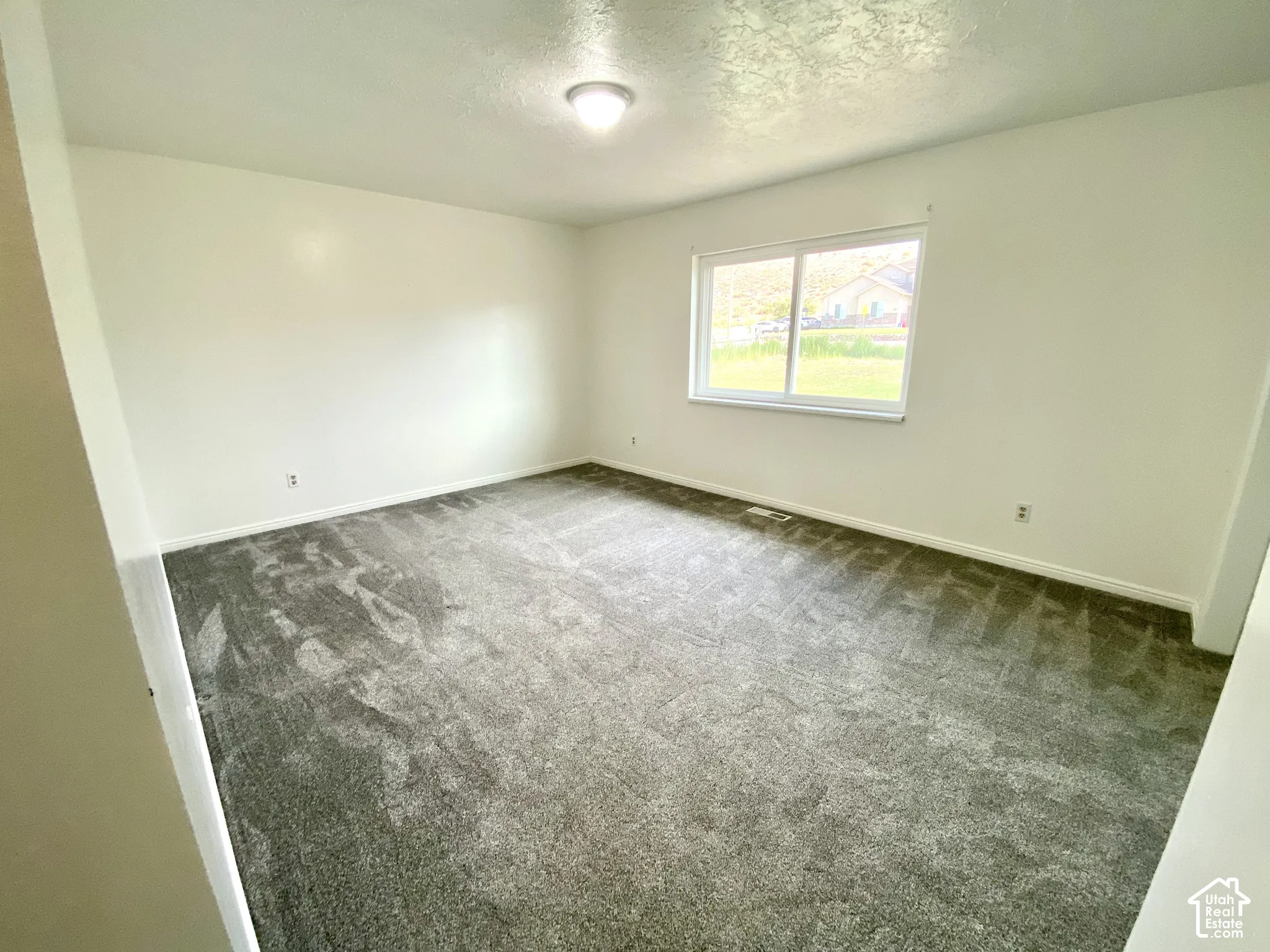 Neutral interior space featuring grey wall-to-wall carpeting, crisp white wall finishes, a sliding window, and a ceiling-mounted light fixture