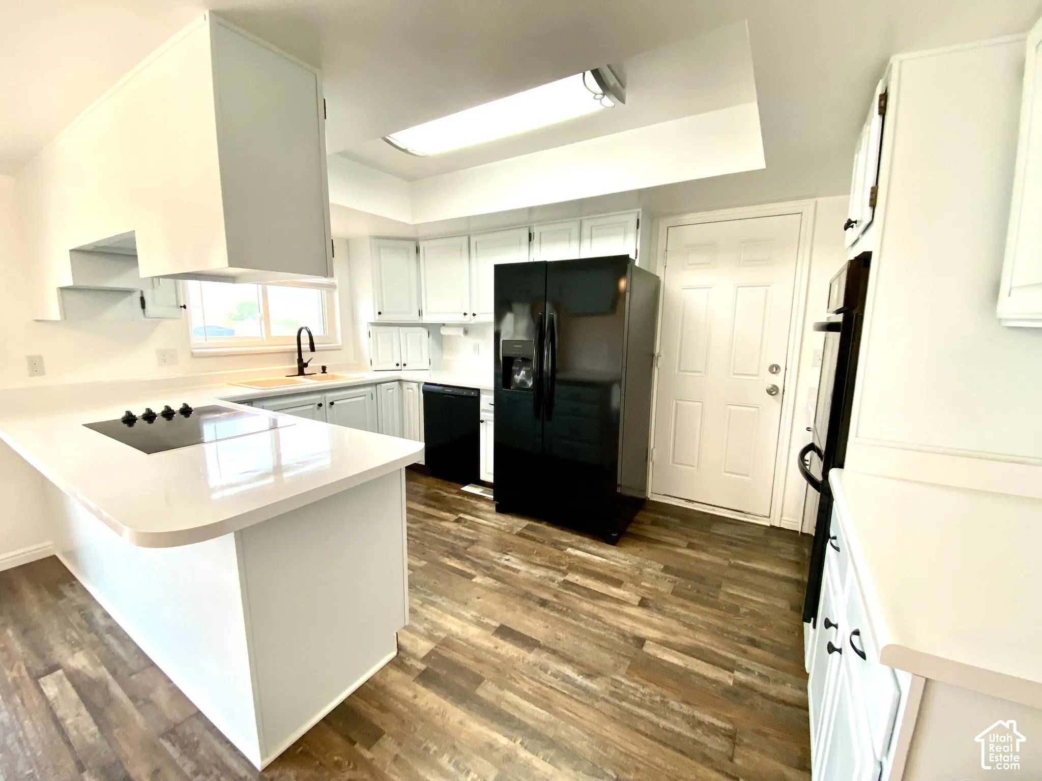 Kitchen featuring solid-surface countertops, wood-finish flooring, recessed lighting, white cabinetry, and integrated appliances