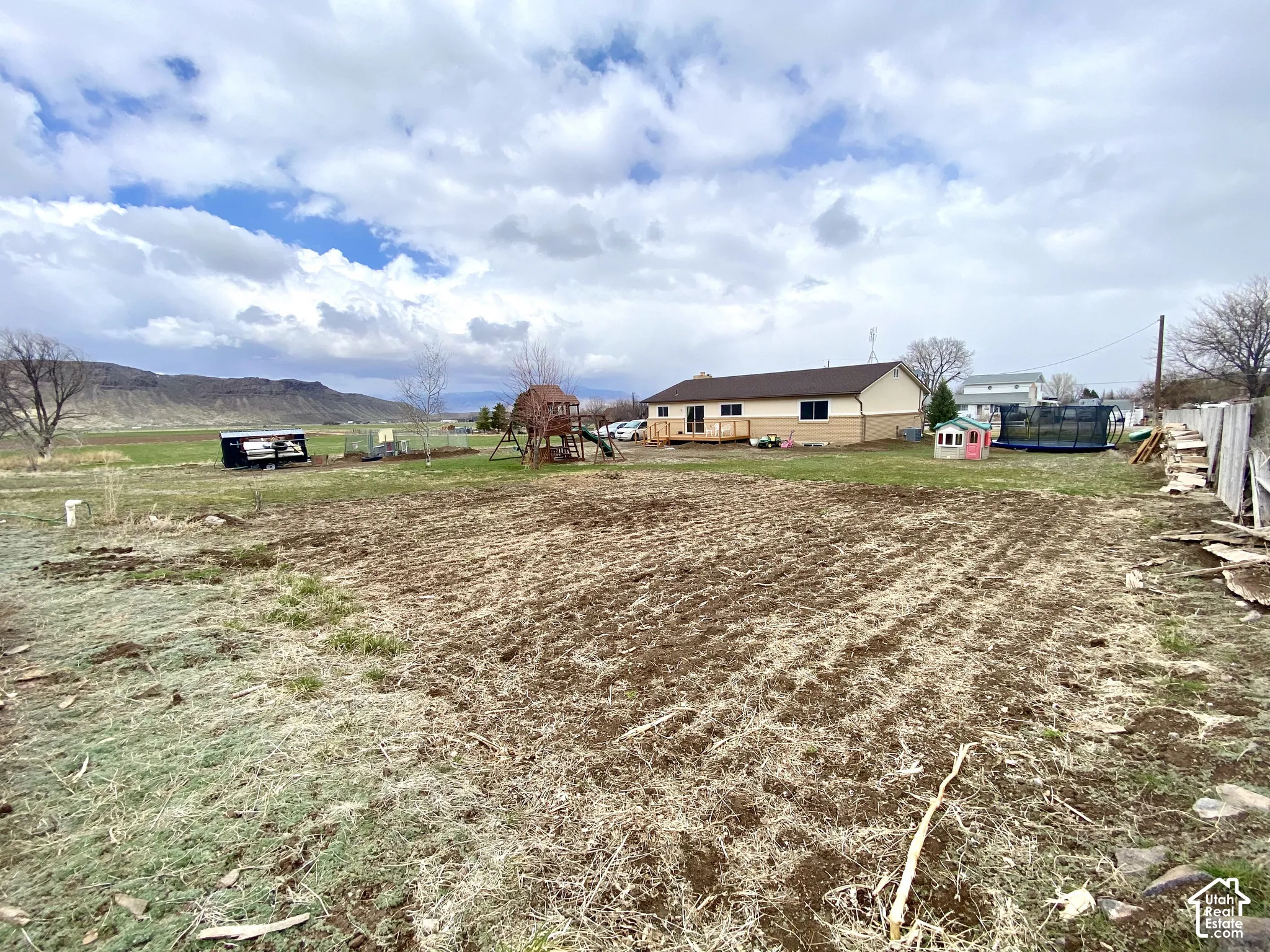 Expansive grounds featuring a tilled garden area, wood-plank deck, and mountain backdrop