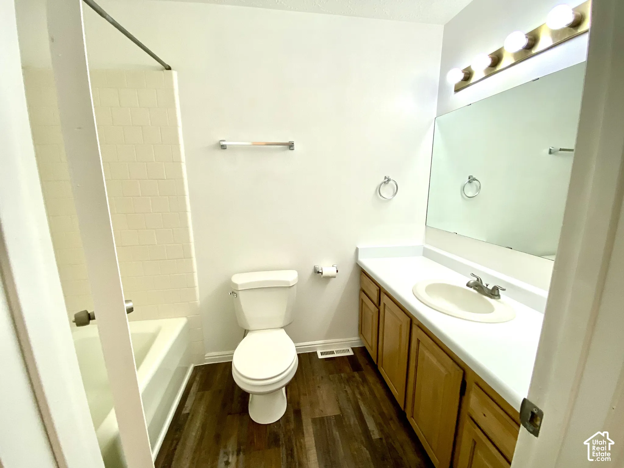 Bathroom featuring a wood-finish floor, a vanity with a white countertop and oval sink, a large wall-mounted mirror, a four-light fixture, and a tub-shower combination with tile surround