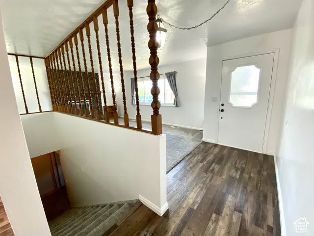 Entryway featuring wood-finish flooring, a turned-wood balustrade, a white front door with decorative glass paneling, and a hanging pendant light