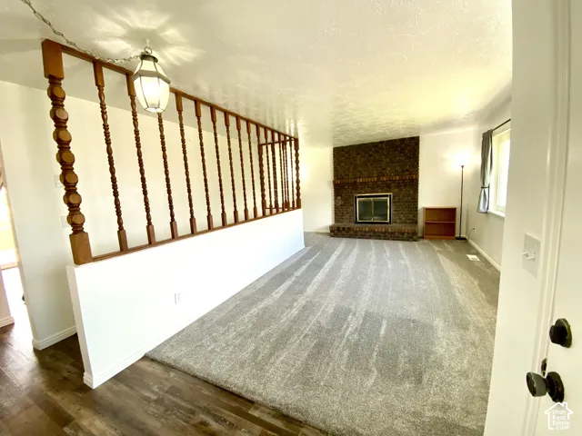 Brick fireplace with a raised hearth, wood-finish flooring, wall-to-wall carpeting, decorative wood spindle room divider, and a hanging pendant light fixture