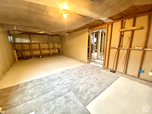 Unfinished lower-level space featuring exposed timber wall studs, built-in wooden shelving, and concrete floor surfacing