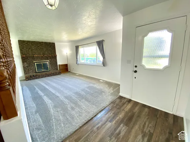 Floor-to-ceiling brick fireplace with metal insert, wood-finish flooring, carpeted area, decorative wood banister, and entry door with glass pane