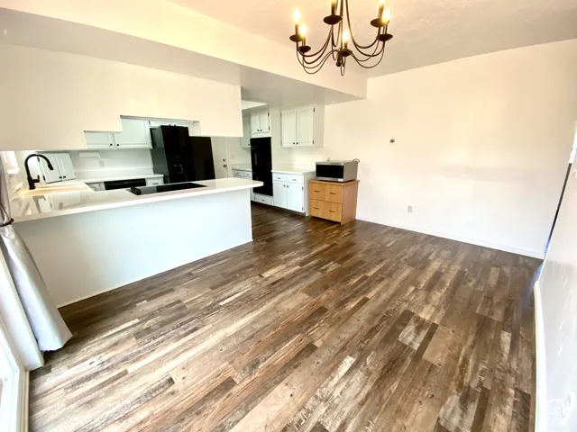 Kitchen featuring wood-finish flooring, white cabinetry, solid-surface countertops, black integrated appliances, and a metal chandelier