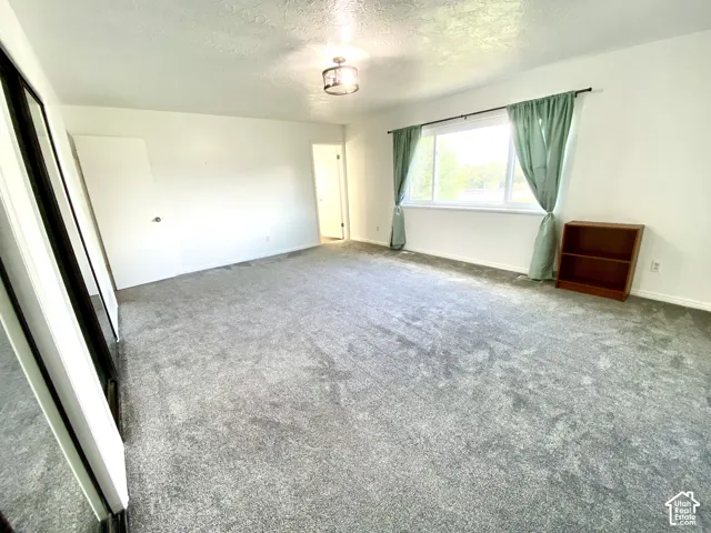 Neutral-toned carpeting, large picture window with natural light exposure, flush-mount drum ceiling fixture, and sliding mirror closet doors