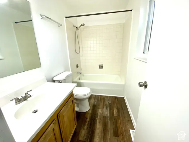 Wood-finish flooring, white vanity with an integrated sink, and a tiled tub-shower combination