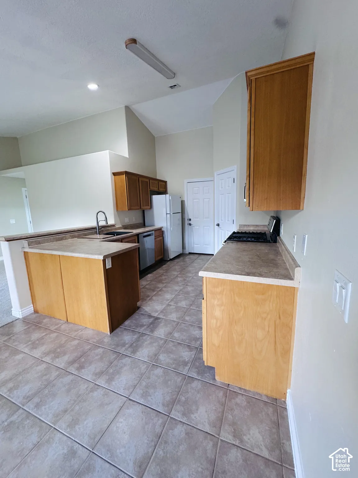 Kitchen featuring wood cabinetry, tile flooring, vaulted ceilings, and a peninsula layout with a built-in sink