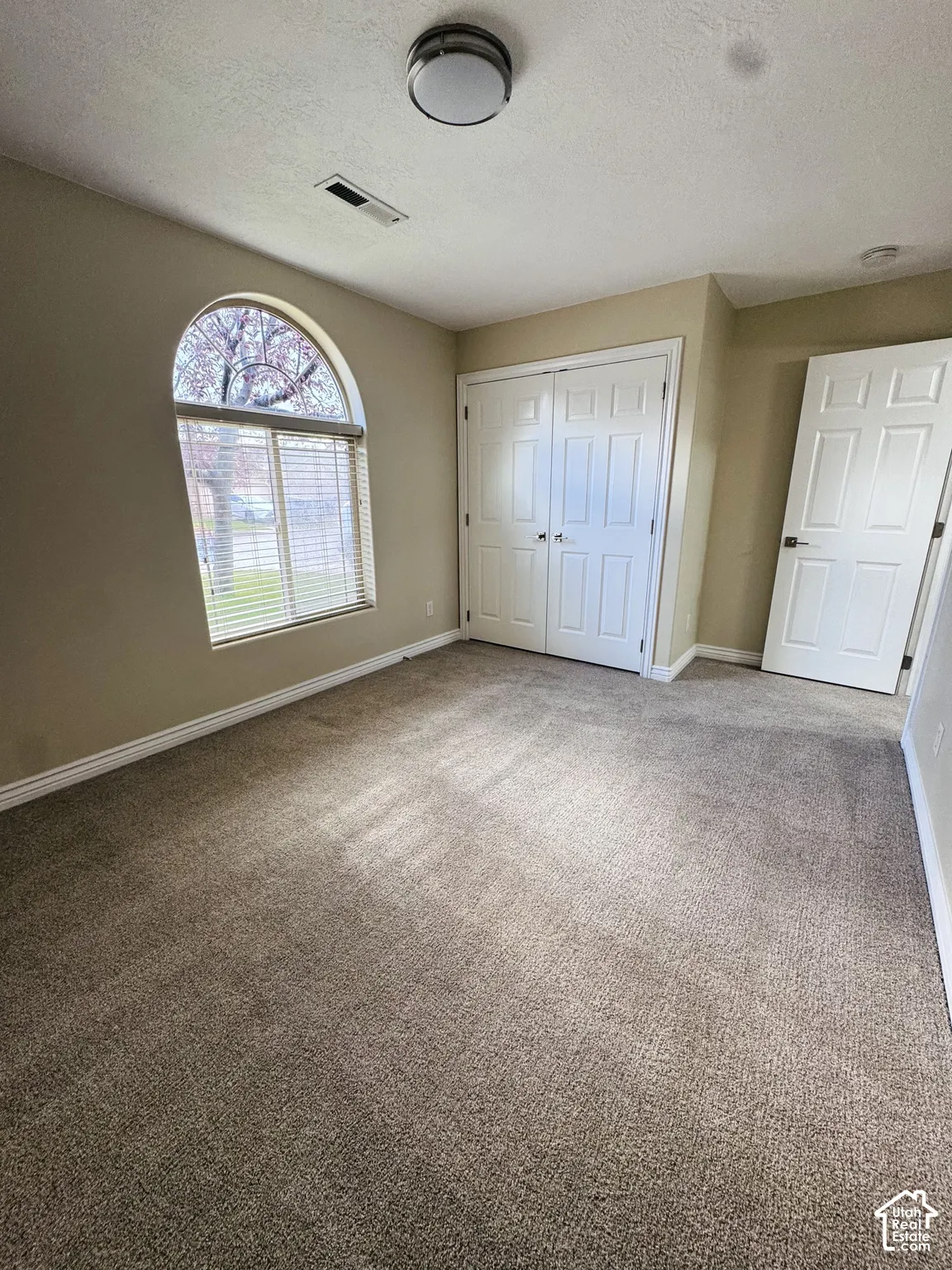 Interior room featuring carpeting, an arched window, double-panel closet doors, a swing door, and a flush-mount ceiling light fixture
