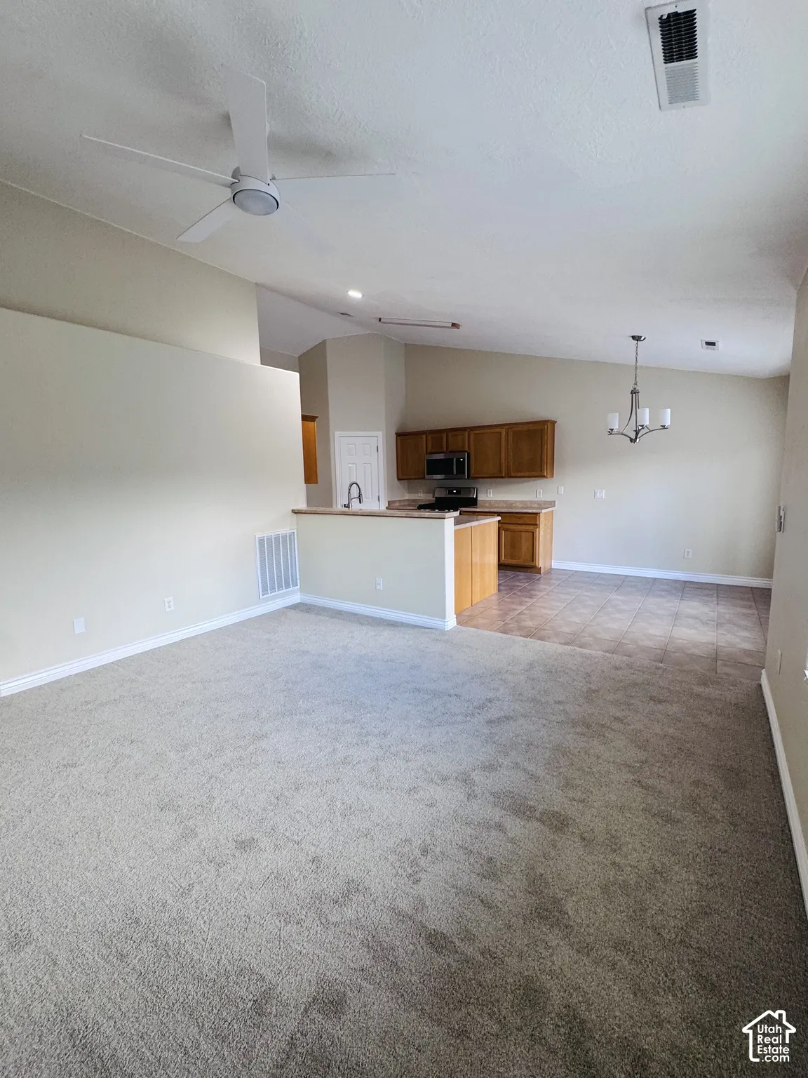 Vaulted ceilings featuring a white ceiling fan and overhead lighting, complemented by tile flooring and wall-to-wall carpeting