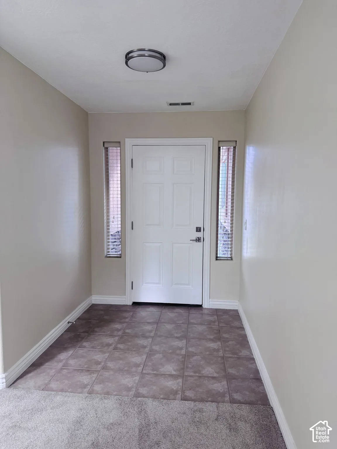 Entryway featuring a white six-panel door, dual vertical sidelight windows with integrated blinds, square tile flooring, and a circular flush-mount ceiling fixture