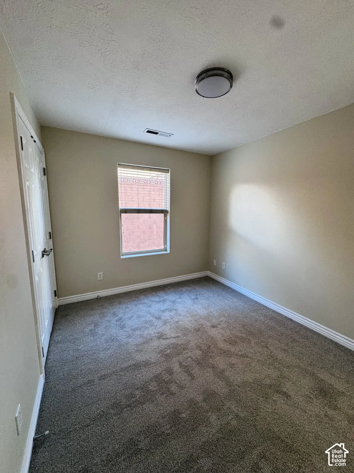 Neutral-toned interior room featuring wall-to-wall carpeting, a multi-panel door, and a single window with blinds
