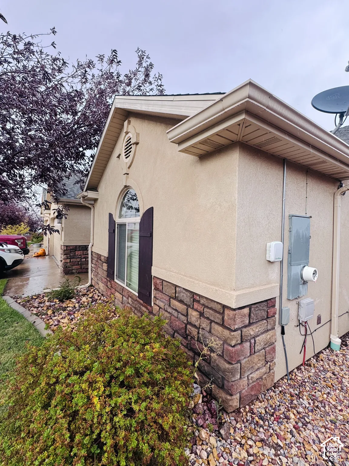 Stucco exterior featuring stacked stone veneer accents, arched window with decorative shutters, and gable roofline
