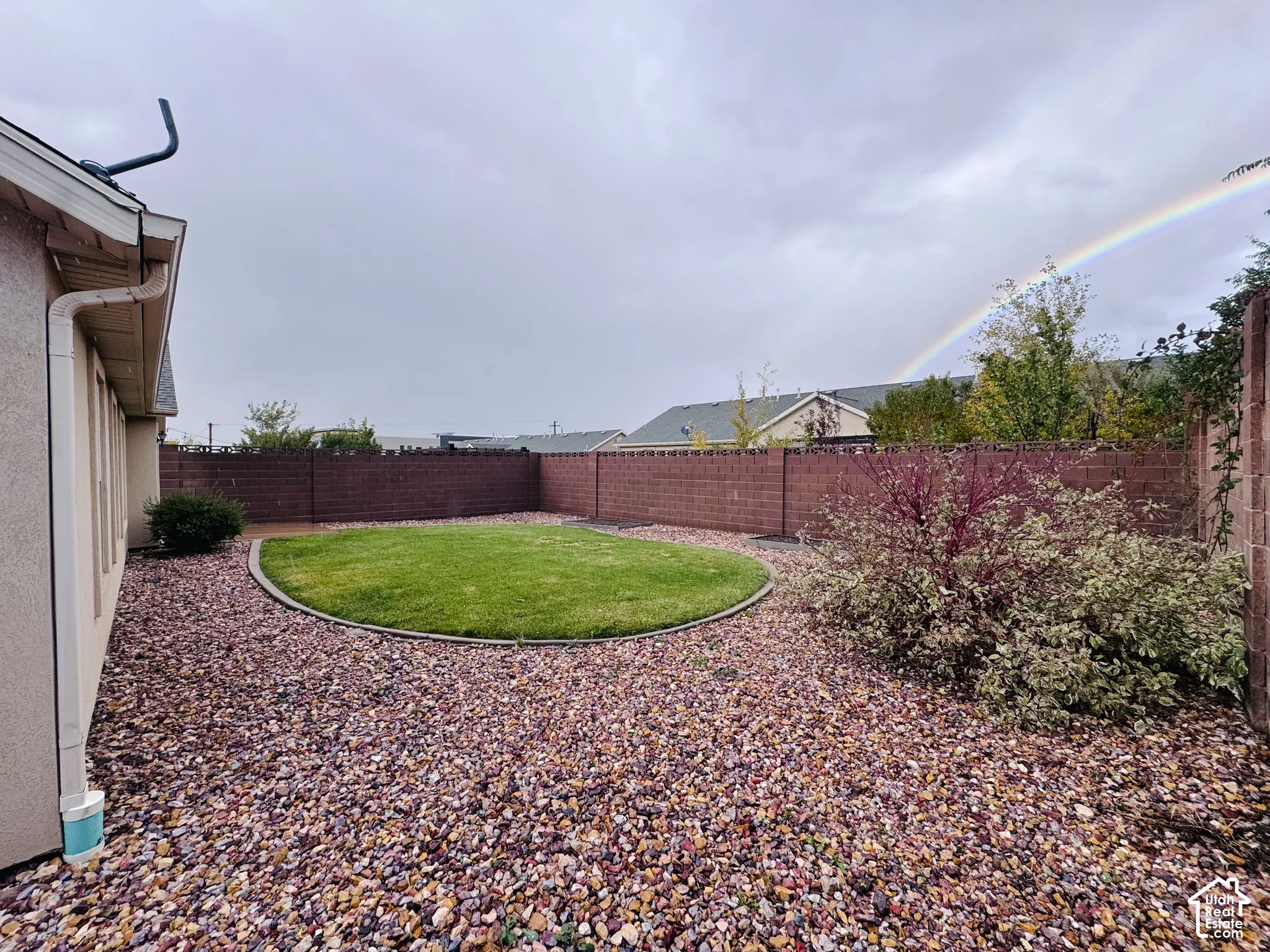 Private backyard featuring a circular lawn, decorative stone ground cover, and a masonry perimeter wall