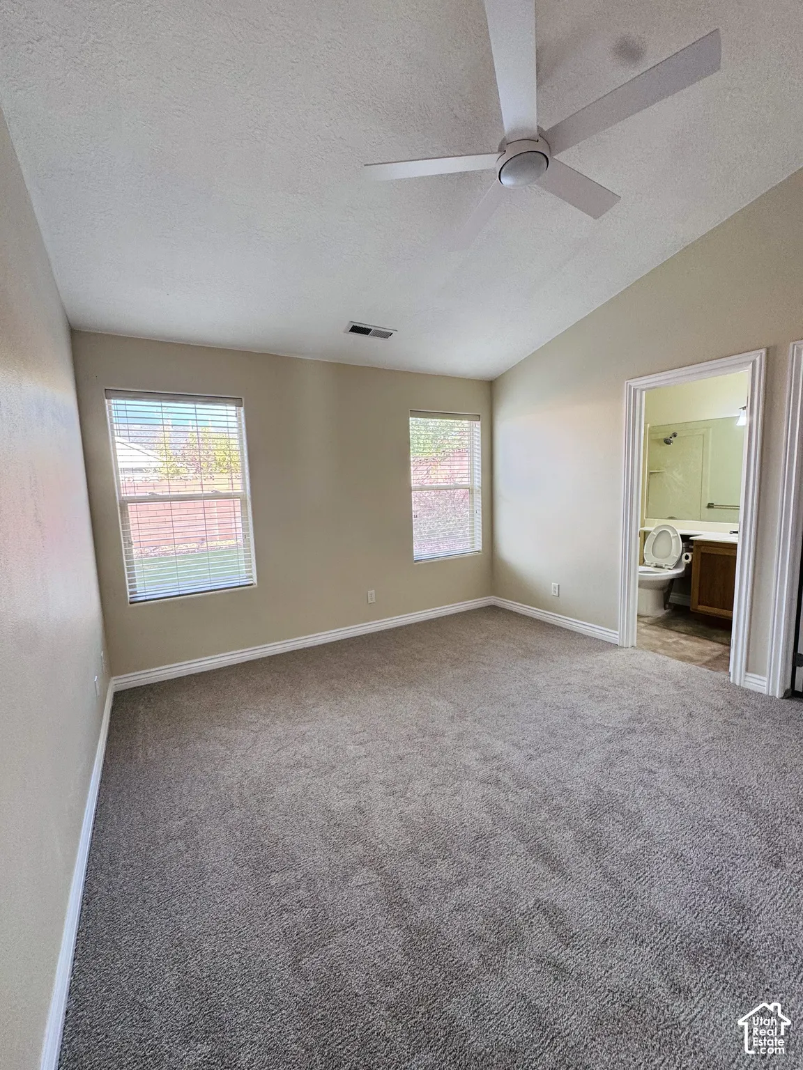 Vaulted ceilings, neutral wall tones, carpeted flooring, two dual-pane windows, and a modern ceiling fan