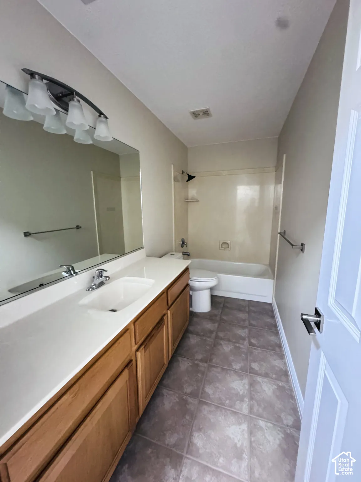 Full-width vanity with an integrated sink, neutral stone-finish countertop, wood-toned cabinetry, and large-format floor tiling