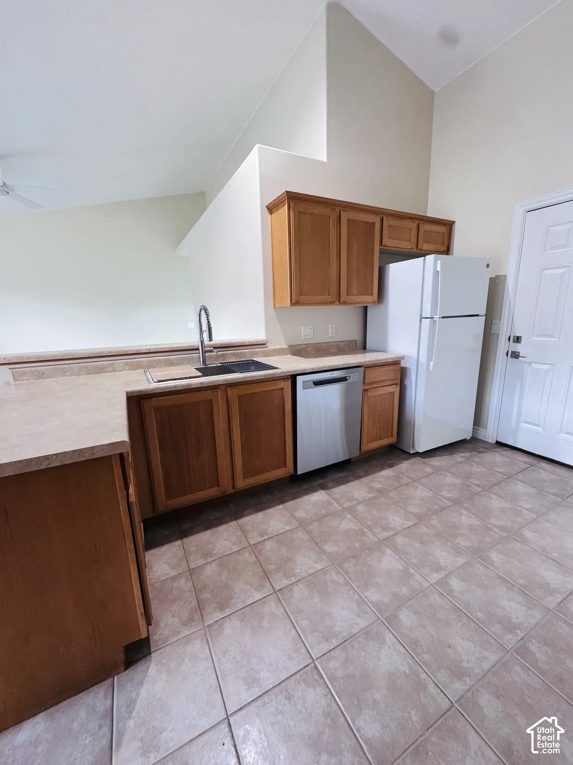 Kitchen featuring wood cabinetry, stainless steel dishwasher, high-arching faucet, laminate countertops, and ceramic tile flooring