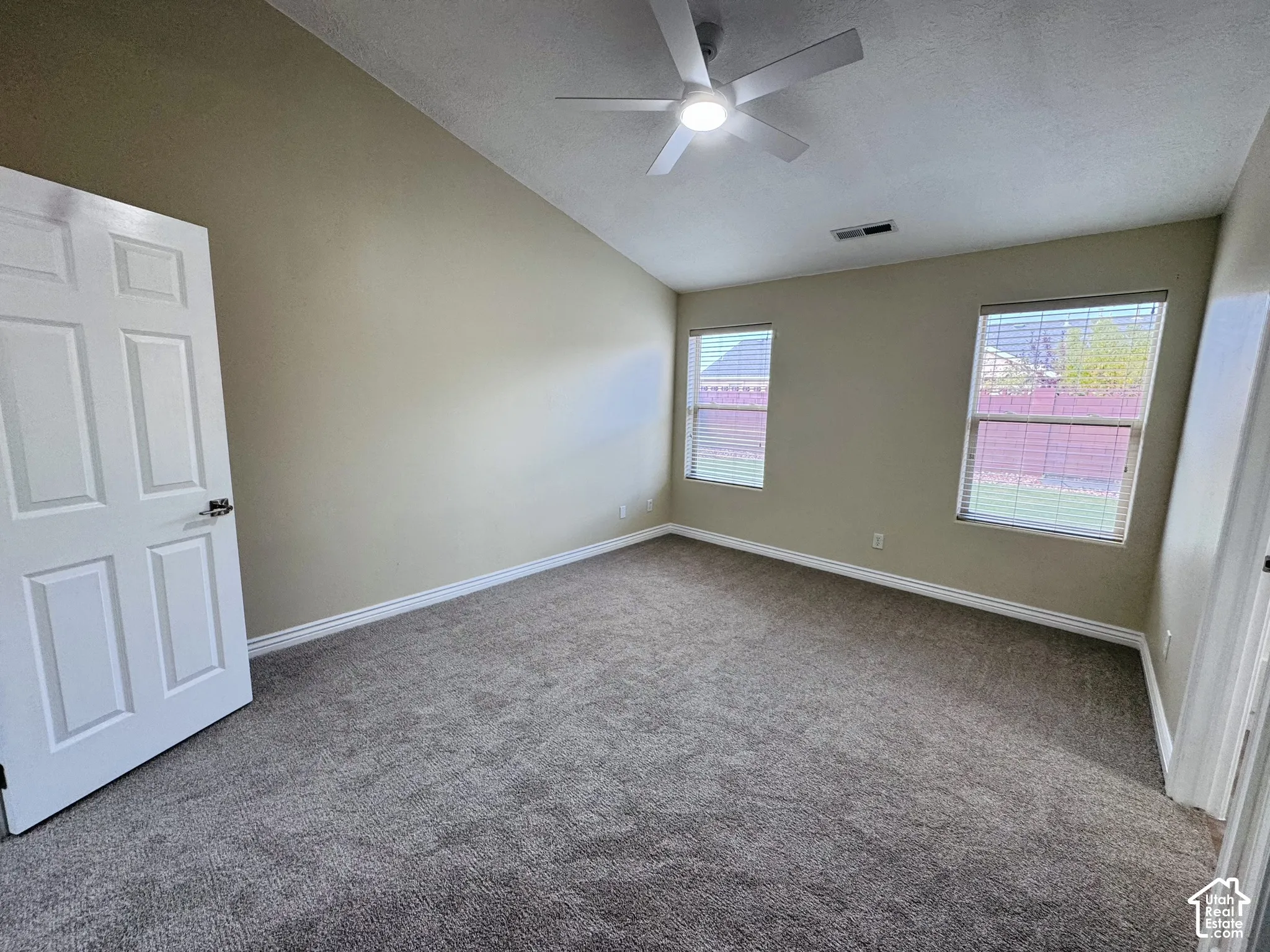 Vaulted ceiling with a centrally mounted ceiling fan, neutral carpeting, and dual windows with blinds