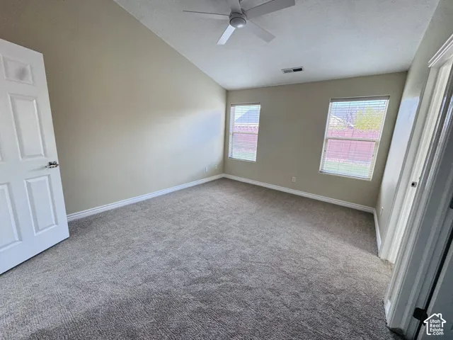 Vaulted ceiling featuring a ceiling fan, neutral carpeting, and two windows providing natural light