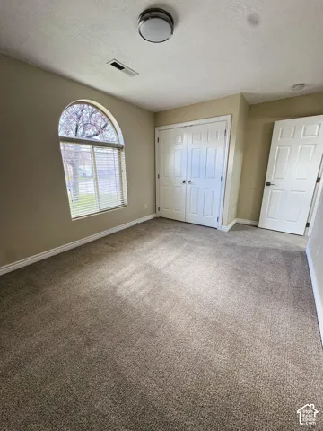 Interior room featuring carpeting, an arched window, double-panel closet doors, a swing door, and a flush-mount ceiling light fixture