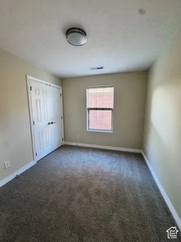 Neutral-toned interior featuring wall-to-wall carpeting, a double-door closet, a single window with blinds, and a flush-mount ceiling light fixture