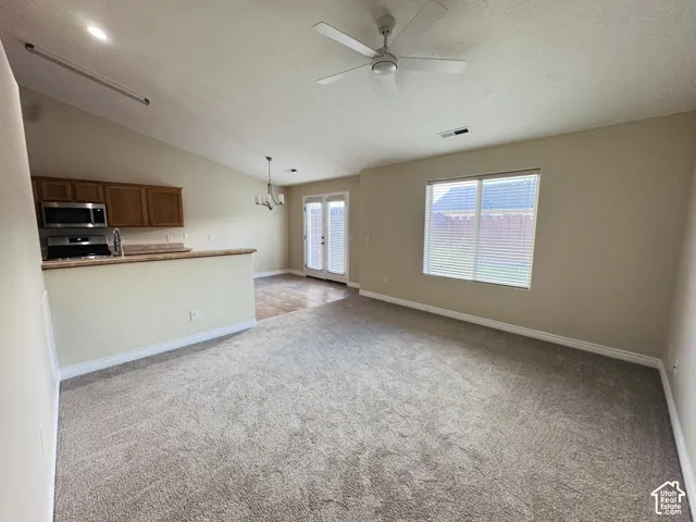 Open-concept interior featuring vaulted ceilings, a ceiling fan, carpeted flooring, a pass-through kitchen counter, and double glass-paned doors