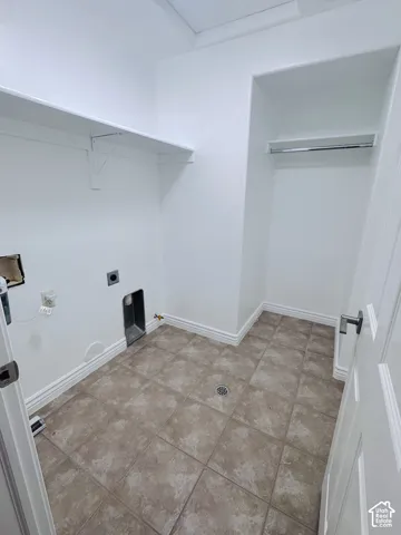 Utility space featuring ceramic tile flooring, built-in shelving, a recessed hanging rod, and dedicated hookups for laundry appliances