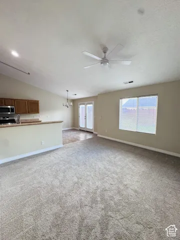 Open interior featuring vaulted ceilings, a ceiling fan, dual glass-paned doors, and cabinetry with a stone-surface countertop