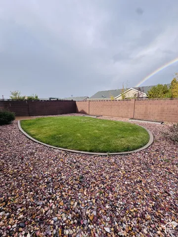 Backyard featuring a central oval lawn, concrete curbing, decorative rock ground cover, perimeter masonry wall, and built-in raised garden beds
