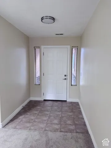 Entryway featuring a white six-panel door, dual vertical sidelight windows with integrated blinds, square tile flooring, and a circular flush-mount ceiling fixture