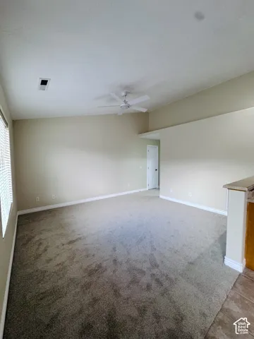 Room featuring vaulted ceilings, neutral wall tones, wall-to-wall carpeting, and a ceiling fan