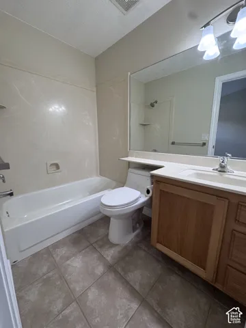 Bathroom featuring a wood-finish vanity with a light-toned countertop, a full-width wall mirror, a ceramic tile floor, and a combination tub and shower enclosure with surround paneling