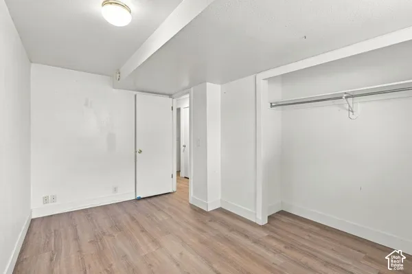 Room featuring wood-finish flooring, white walls, built-in closet with overhead rack, and flush-mount ceiling lighting