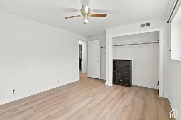 Interior room featuring wood-finish flooring, white walls, and a ceiling fan with light fixture
