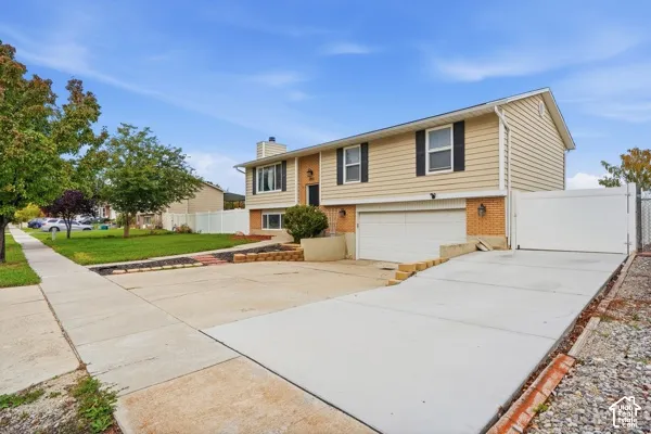 Split-level exterior featuring light-toned horizontal siding, a brick lower-level facade, integrated two-car garage, concrete driveway, and white vinyl privacy fencing