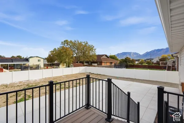 Backyard featuring a composite deck with black metal railing, concrete patio, white vinyl perimeter fencing, and mountain scenery