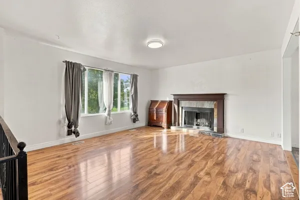 Living area featuring wood-finish flooring, a fireplace with a wood mantel and stone surround, and large windows