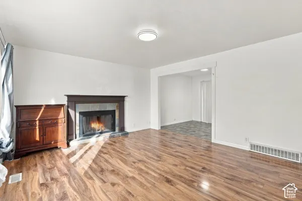 Living area featuring wood-finish flooring, a fireplace with a dark-finish mantel, and stone-tiled hearth