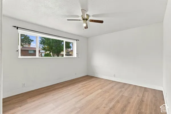 Room featuring wood-finish flooring, a large picture window, and a ceiling-mounted light fixture with a multi-blade fan