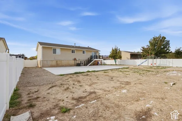 Rear exterior featuring horizontal siding, elevated deck with railing, concrete patio, and full-perimeter vinyl fencing