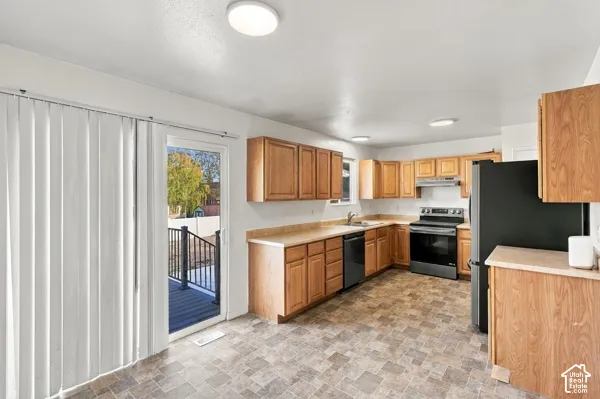 Kitchen featuring wood cabinetry, laminate countertops, integrated range with overhead hood, and sliding glass door with exterior deck access